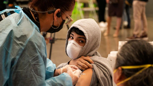 a student looks back at his mother as he is vaccinated