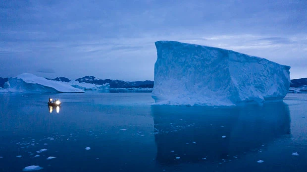 A boat navigates at night next to large iceberg