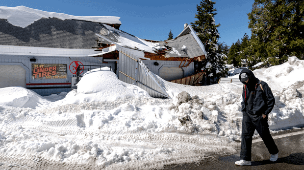 A man walks past a damaged tire shop in Crestline, Calif., Friday, March 3, 2023, following a huge snowfall that buried homes and businesses. (Watchara Phomicinda/The Orange County Register via AP)